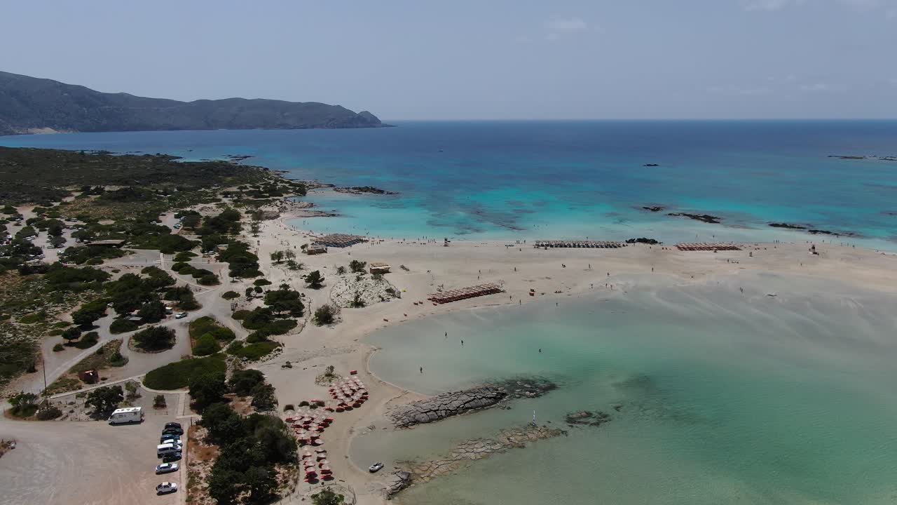 Elafonissi Beach in Crete Greece with vehicles in the arrival parking area, Aerial pan left shot