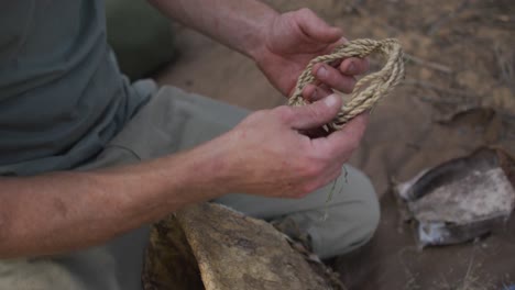 caucasian male survivalist preparing tinder from twine to make fire at camp in wilderness