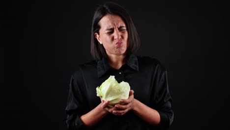 mujer joven mordiendo repollo con mala expresión facial, concepto de comida vegana saludable, fondo negro