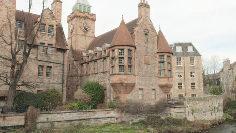 Pan-up-from-the-Water-of-Leith-river-to-Dean-Village-Well-Court-and-clock-tower-on-an-overcast-day-in-Edinburgh,-Scotland