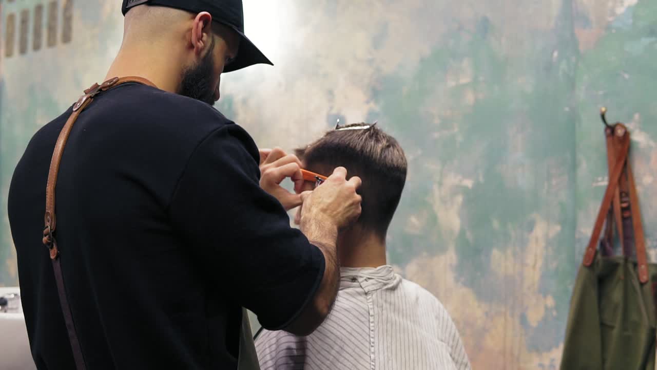 joven hombre caucásico guapo que se corta el cabello en un barbero moderno. peinado con un cortador eléctrico por un barbero barbudo