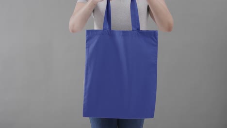 caucasian woman wearing white t-shirt holding blue bag on grey background, copy space, slow motion