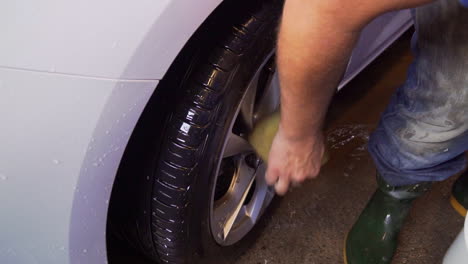 trabajador rociando agua y lavando la llanta y las ruedas, de un automóvil todoterreno blanco, en un lavadero de automóviles, en suecia