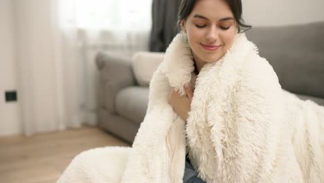 portrait of young beautiful woman in warm fur blanket at home