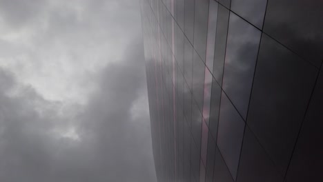Dark,-cloudy-sky-reflected-in-a-dark-glass-building