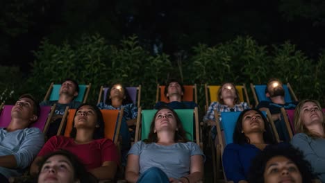 a group of friends enjoying a relaxing evening under the stars, reclining in colorful chairs while watching a movie with lights illuminating their faces