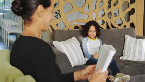 side view of caucasian woman reading magazine and african american boy using digital tablet on sofa