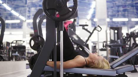 Attractive-young-blond-caucasian-woman-with-sporty-body-smiling-while-exercising-on-leg-press-mashine-at-the-gym.-Healthy-lifestyle-concept.