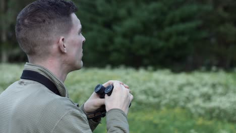 close up of a man in the wilderness looking at a distance through binoculars