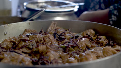 chef adding fried onions and placing fresh cut lemons onto meat curry dish in kitchen