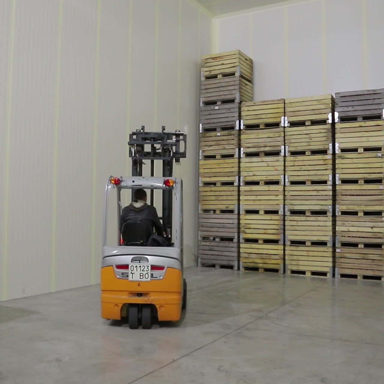 A warehouse worker carries wooden boxes of apples and stacks them in rows together near the wall of the room. Juice factory.