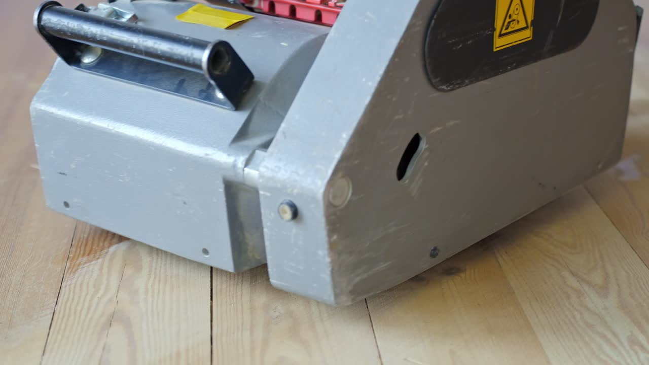 Close-up view shows a professional floor sanding machine working on a pine wood floor, revealing the sharp transition between sanded and unsanded wood, camera low, slow motion, smooth linear movement.