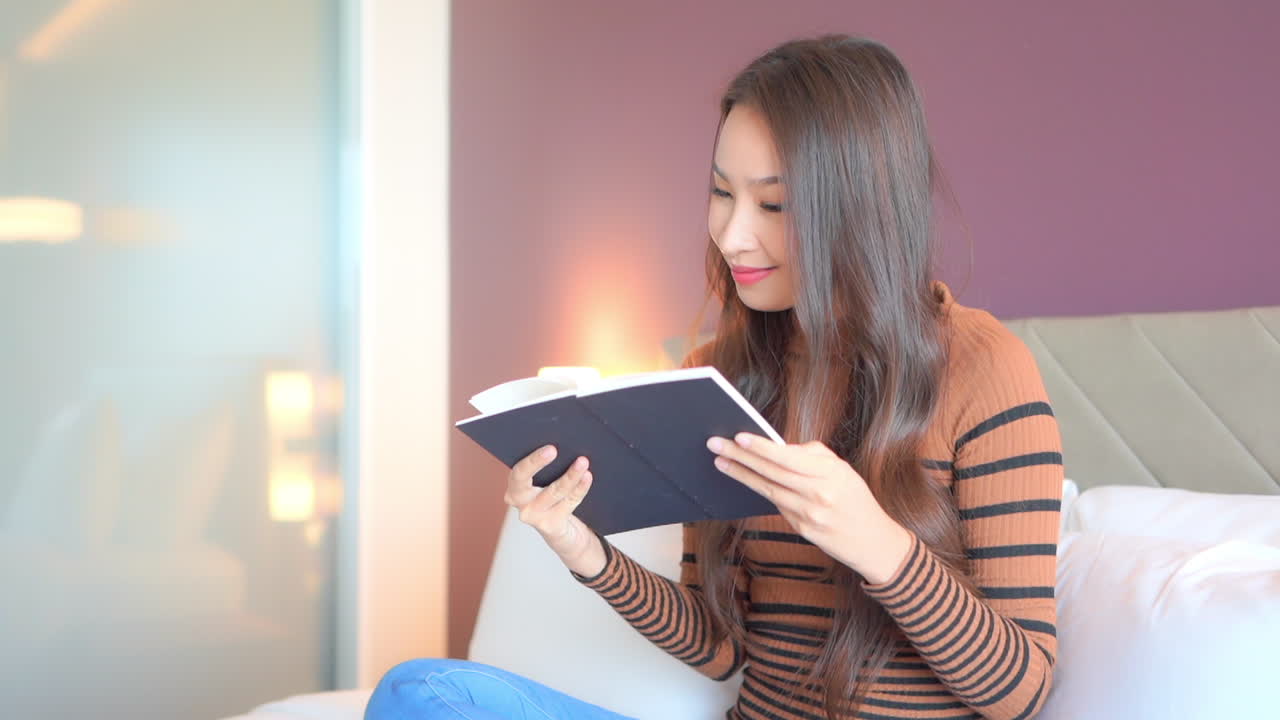ベッドの上で足を組み、試験勉強をするアジア人女子学生
