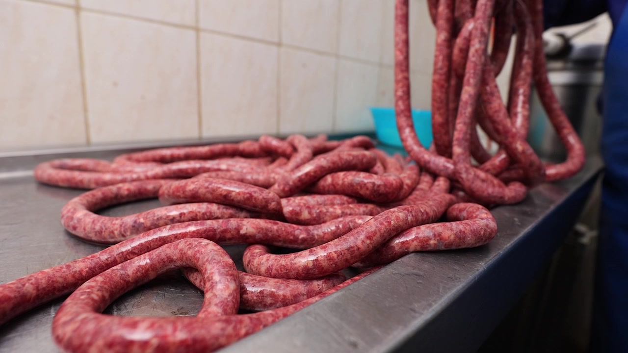 Long rope of raw sausage coiled onto stainless steel workbench table