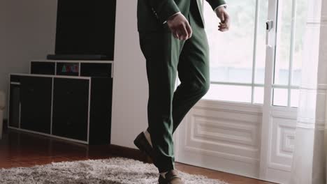 Un-Hombre-Con-Traje-Verde-Caminando-En-El-Interior-Sobre-Una-Alfombra-Lujosa-Cerca-De-Una-Ventana-Grande,-En-Una-Habitación-Moderna