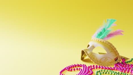 video of masquerade mask with feathers and mardi gras beads on yellow background with copy space