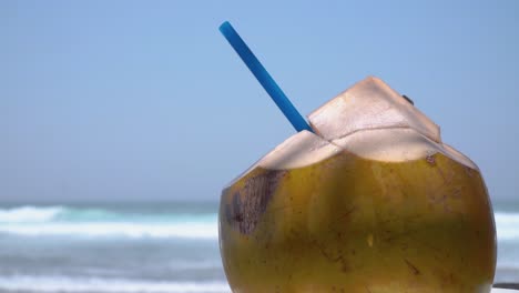 fresh coconut drink with blue straw on the beach with sea background