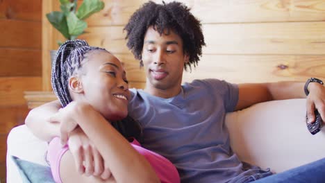 feliz pareja afroamericana viendo televisión, sentada en el sofá en una cabaña de madera, cámara lenta