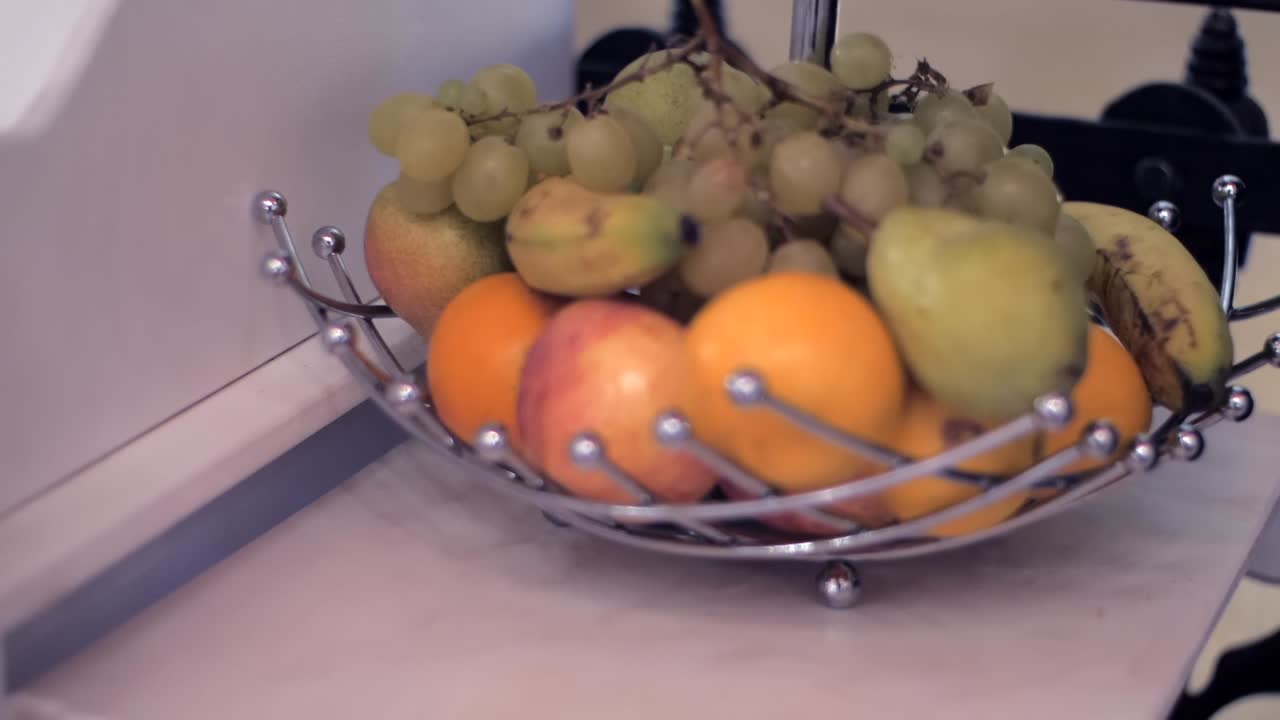 Close-up handheld view of assorted fruits in a modern metal basket at home.