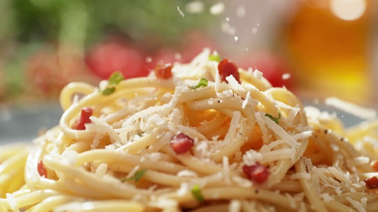 raspar el queso en un plato recién preparado, servirlo en un platillo, espagueti carbonara con pancetta, huevo, pimienta negra y hierbas picadas