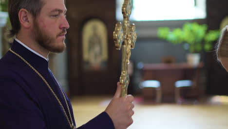 el sacerdote bendice al parroquiano con la santa cruz.