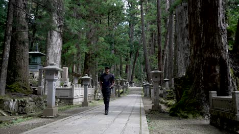 solo male backpacker casually walking along path through zen forest cemetery in japan