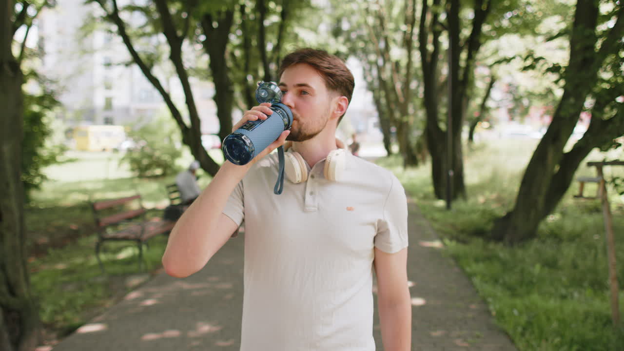 Sporty athletic thirsty man runner jogger drinking water after sport workout in park outdoors