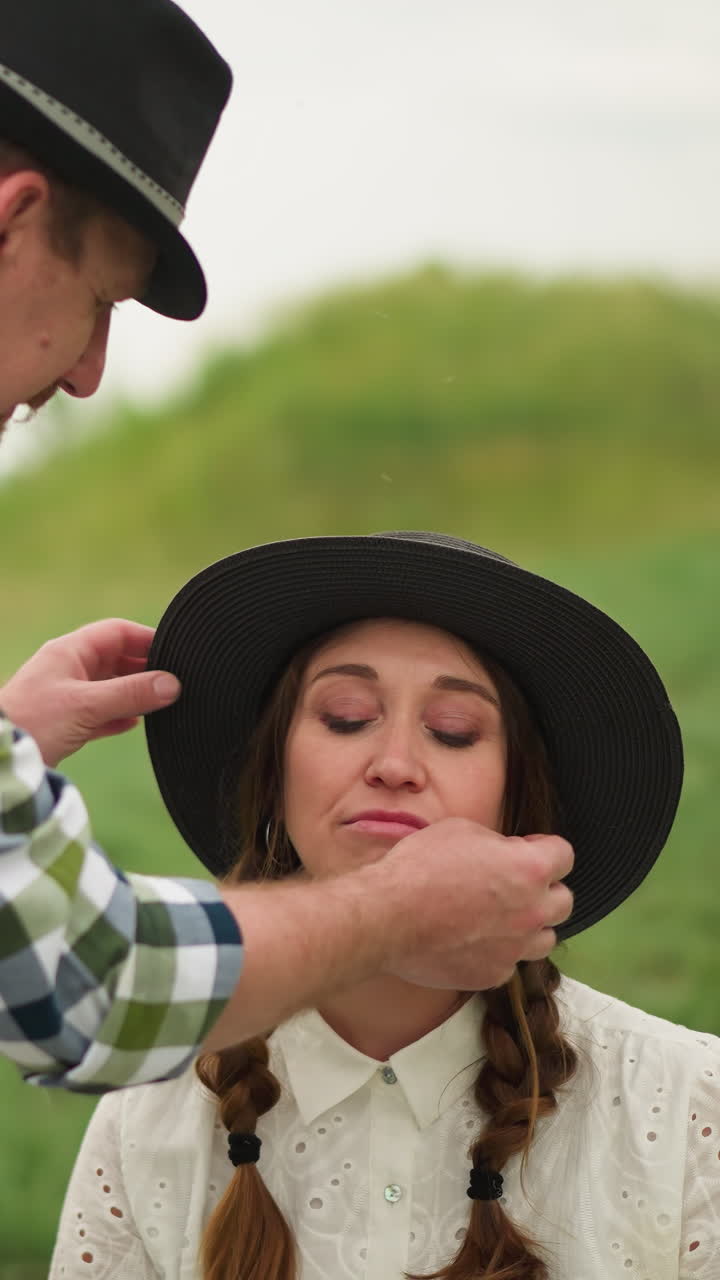 체크 된 셔츠를 입은 예술가는 색 드레스를 입고 녹색 에 앉아 부끄럽게 미소 짓는 머리카락을 가진 여성의 모자를 조정합니다.