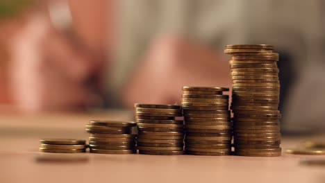 home budget calculation, coin stacks with man in background writing in notebook