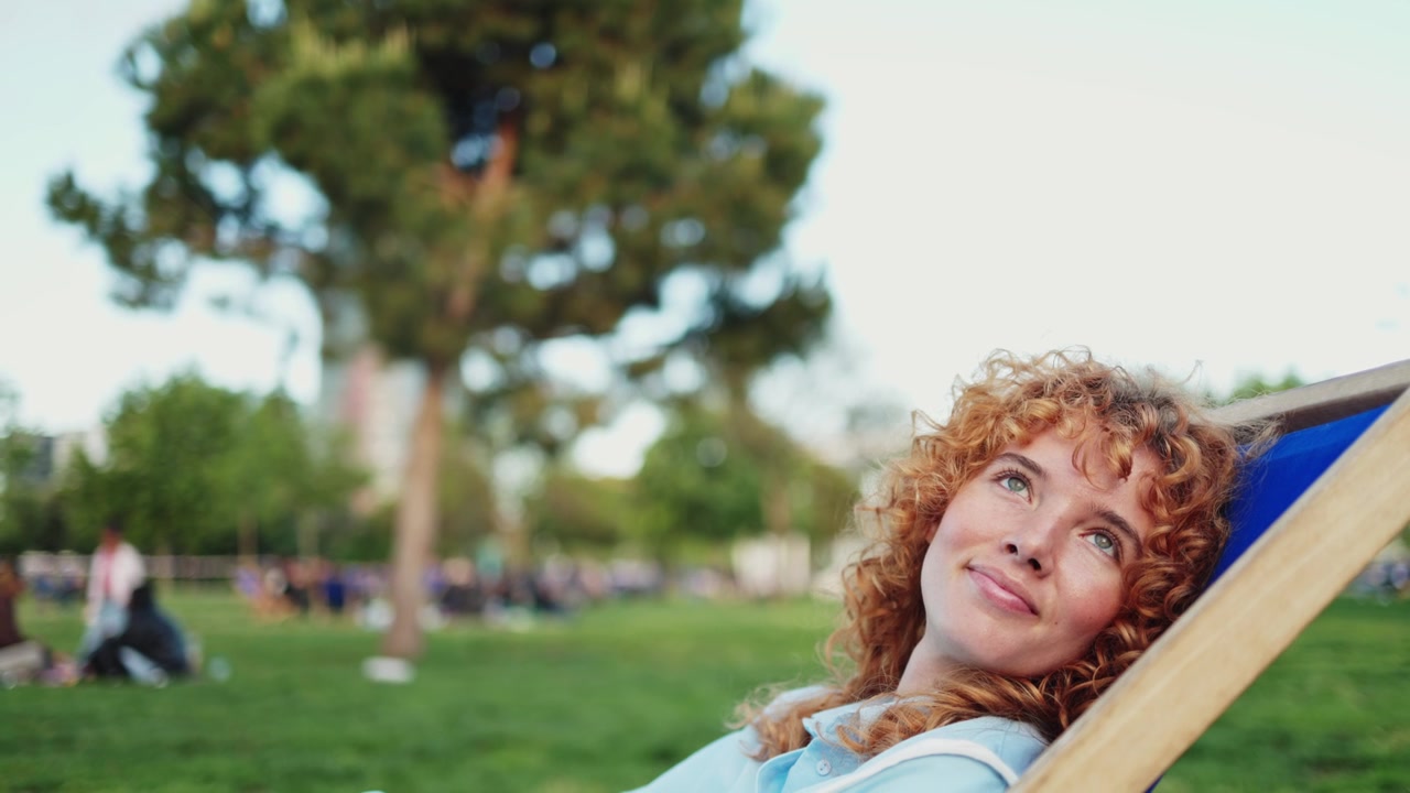 Giovane donna con capelli rossi ricci che si rilassa al parco.