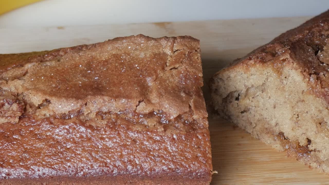 Pan right shot of freshly baked banana bread loaf resting on wooden board with golden crust