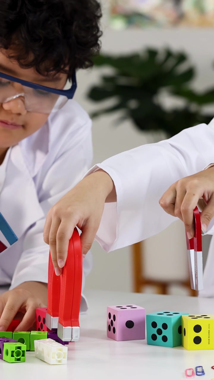 Anak-anak beragam mengenakan jas lab menggunakan magnet untuk menguji balok warna-warni selama pelajaran sains.