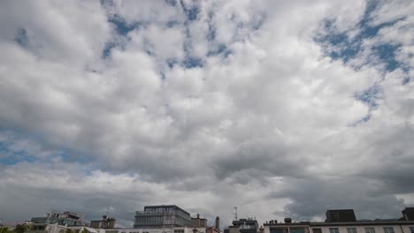 time lapse of fast moving white clouds over urban rooftops against a blue sky