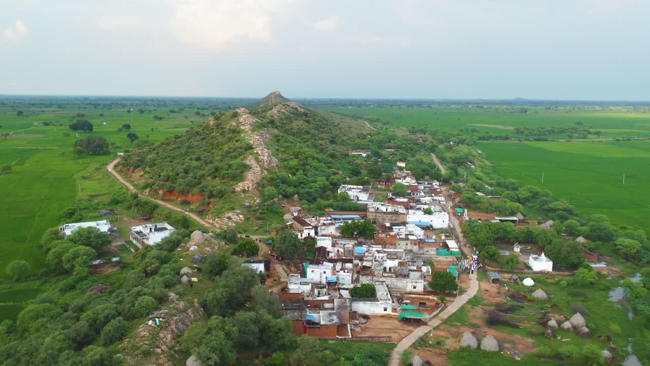 Aerial drone shot of a village under a green hill with paddy fields all around at a small village in ndia