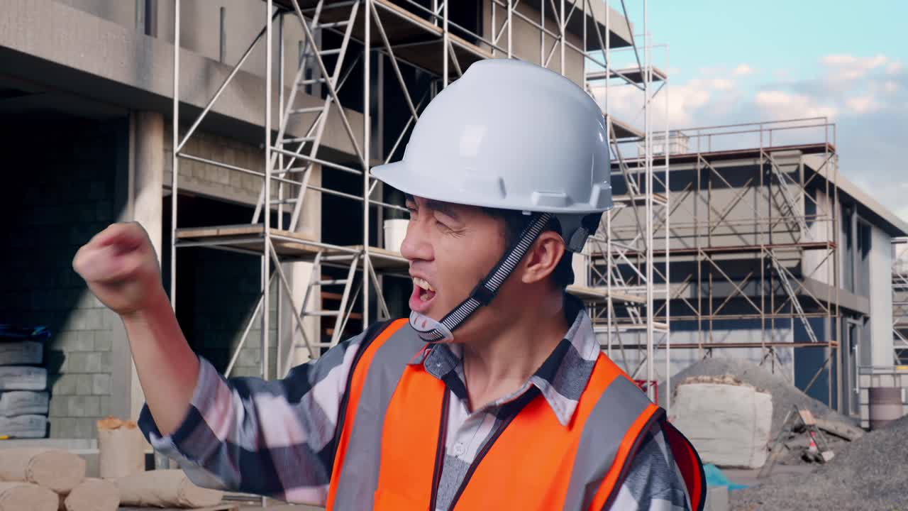 Close Up Side View Of Angry Asian Male Engineer With Safety Helmet Shouting At Someone While Standing At Building & Construction Site in Progress to New House