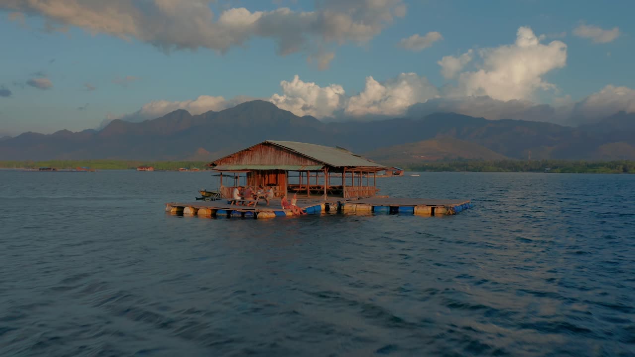 Flying past tropical floating bar out at sea from shore of West Bali, sunset