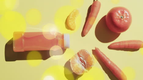 composition of spots of light over bottle of fruit juice, carrots and oranges on yellow background