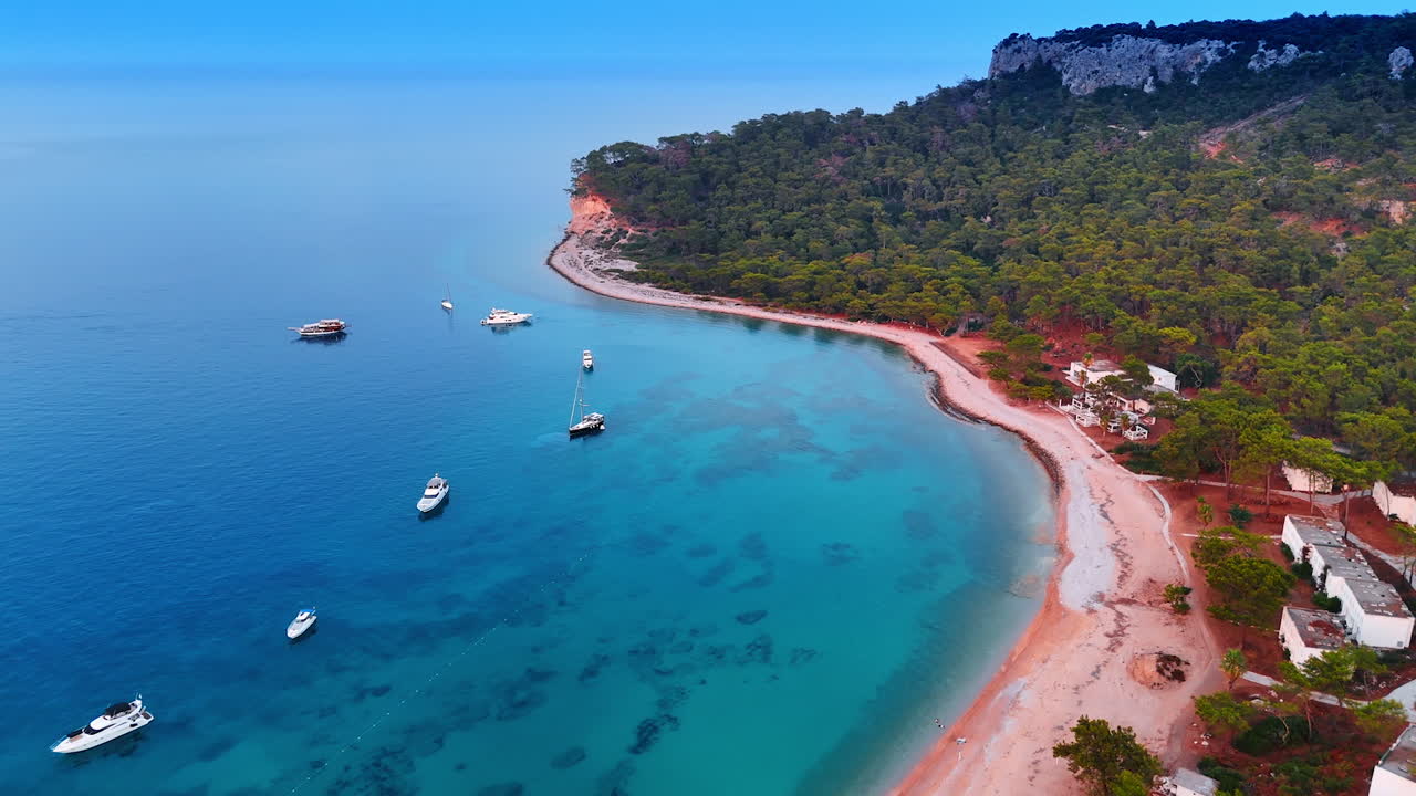 Several yachts stand on the azure clear waterscape near the picturesque shore of Turkey. Green woods cover the rocks at the coast. Aerial view