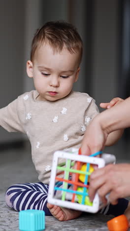 lovely little boy plays with toys sitting on the floor. mommy helps her son to pick up the toy. vertical video