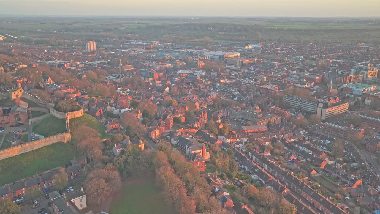 Lincoln city cityscape from an aerial perspective, showing historic Lincoln Castle walls and sprawling urban development bathed in warm, soft light during sunset