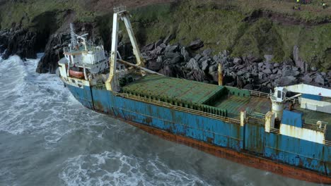 Aerial-drone-shot-of-waves-crashing-into-a-big-abandoned-cargo-ship-on-Ireland’s-south-coast