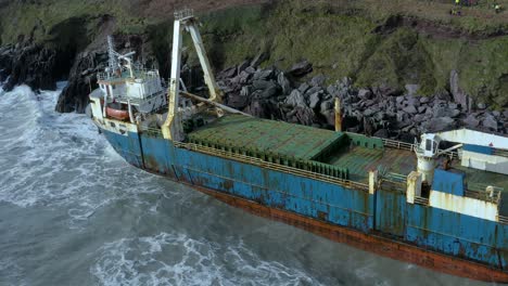 aerial drone shot of waves crashing into a big abandoned cargo ship on ireland’s south coast