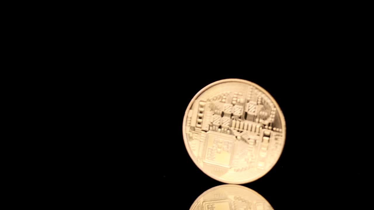 Gold cryptocurrency coin spins and falls, illuminated dramatically against a glossy black background