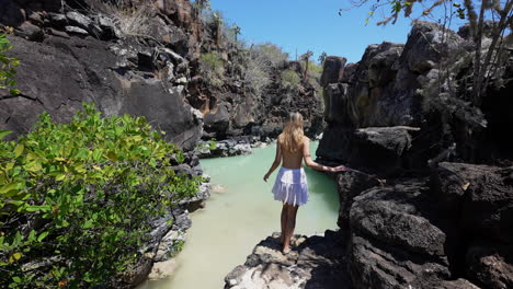 female tourist walking down rock steps to view natural pool at las grietas in santa cruz island, galapagos