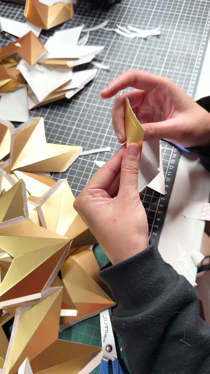 Person hands crafting golden origami stars from metallic cardstock for decoration