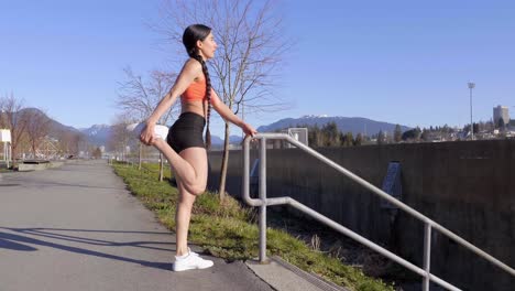 athletic young woman stretching quad muscles of legs holding stair railing