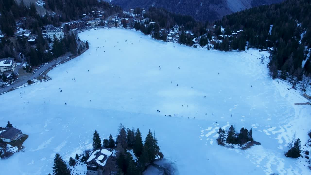 Filmagem aérea com drone de um lago congelado em Champex, Suíça, durante o inverno. Pessoas patinando no gelo cercadas por paisagens alpinas com neve. Filmado em <1>4K</1> usando um DJI Mini 2