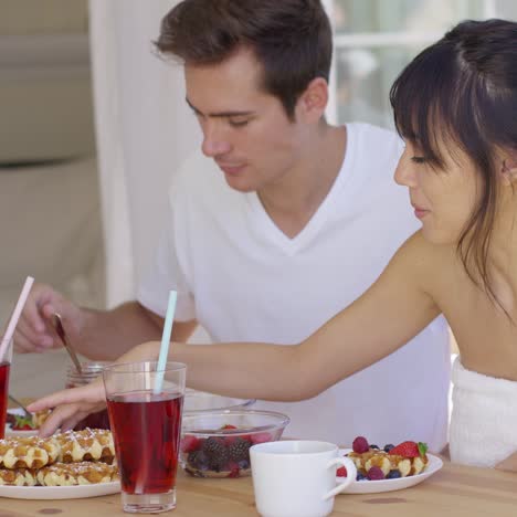 woman trying to feed annoyed man a waffle