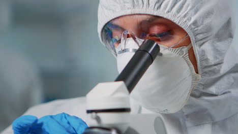 lab technician with protection suit examining samples using microscope