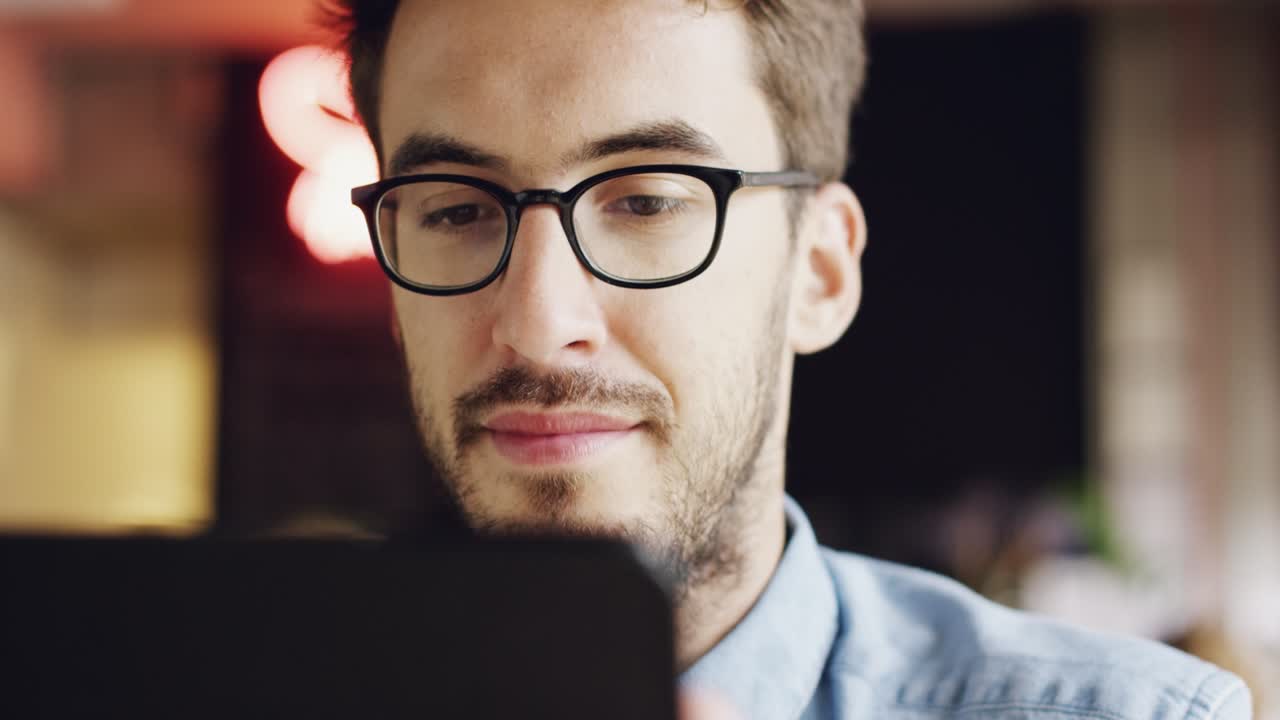 imágenes de video de 4k de un joven guapo sentado solo en un café y usando una tableta digital